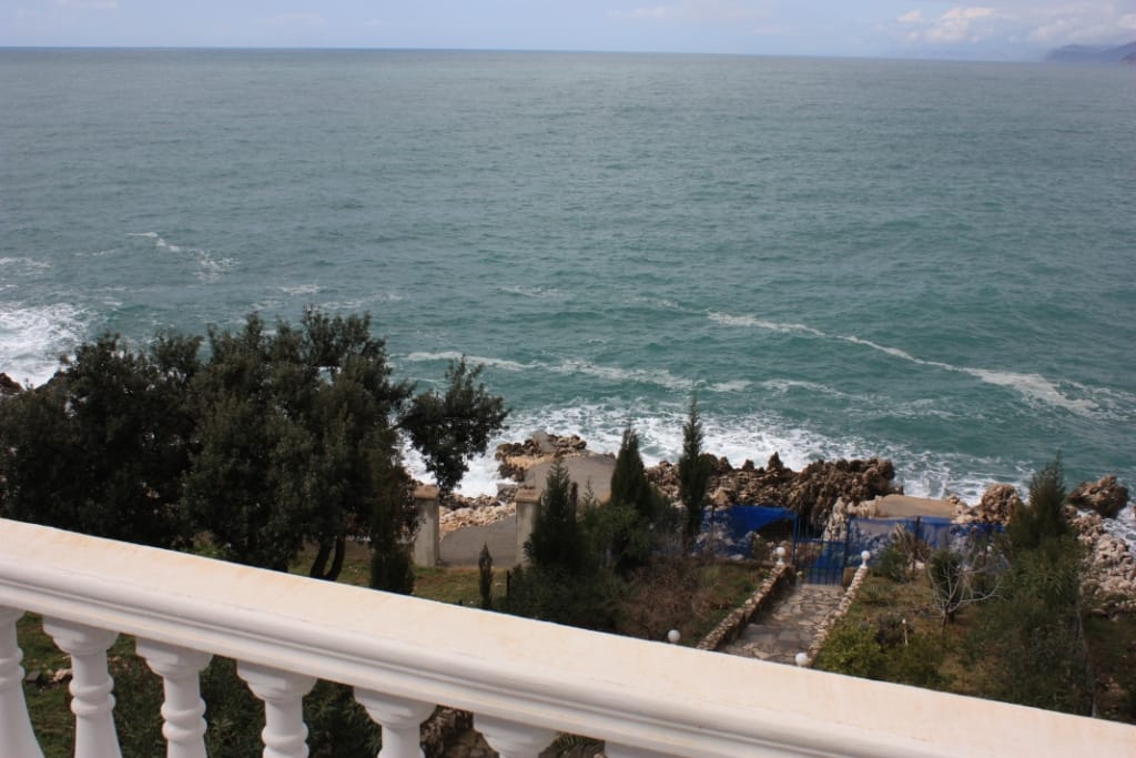 View from the balcony of the sea and rocky shore in a house in Utjeha, Montenegro: white balusters, garden, and direct access to the water.