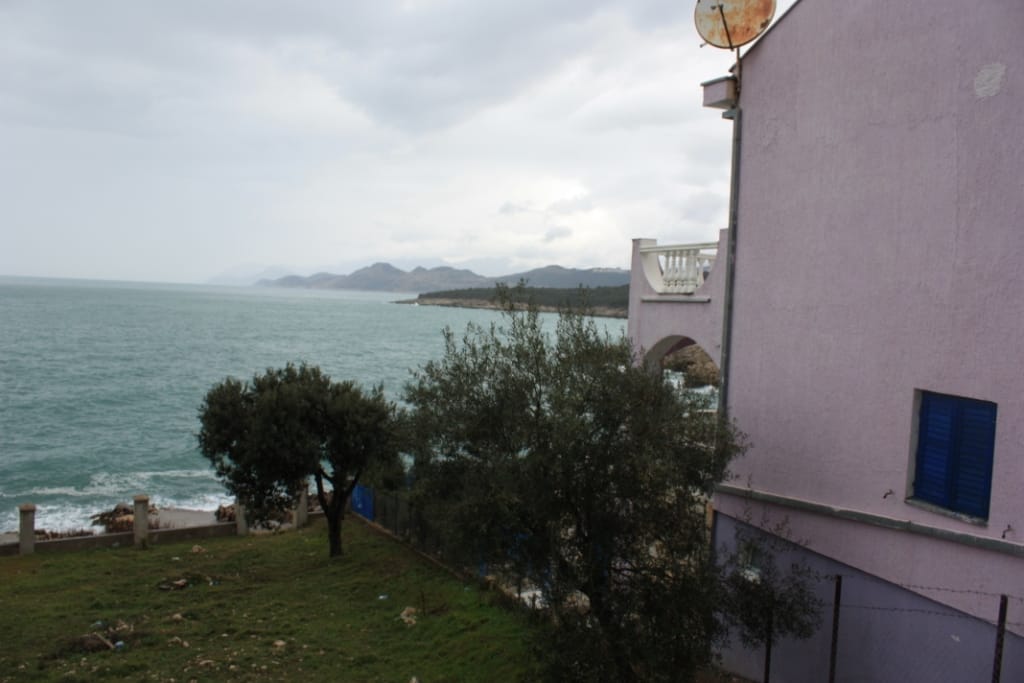 House in Utjeha, Montenegro: sea and coastline view from the terrace of a private house with a pink facade and blue shutters.