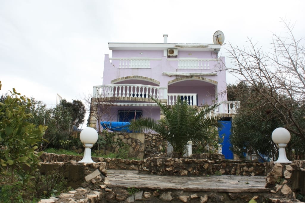 Three-story house with terraces and stone cladding in Uteha, Montenegro, with a garden and a palm tree on the property.