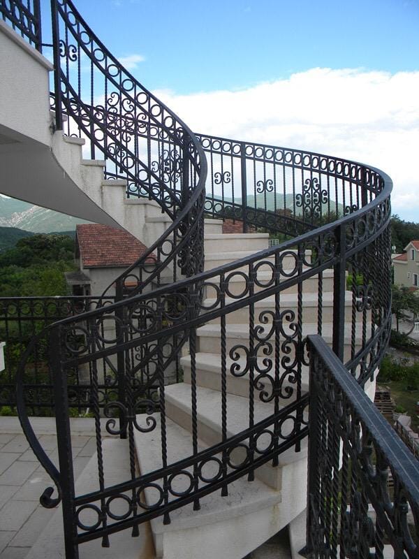 A spiral staircase with wrought-iron railings in a villa in Herceg Novi, Montenegro, with panoramic views of the mountains and the city.