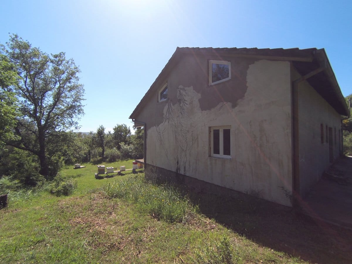 Facade of a private house under finishing with a plot and apiary in Kavaci, Montenegro, overlooking a green garden and trees.