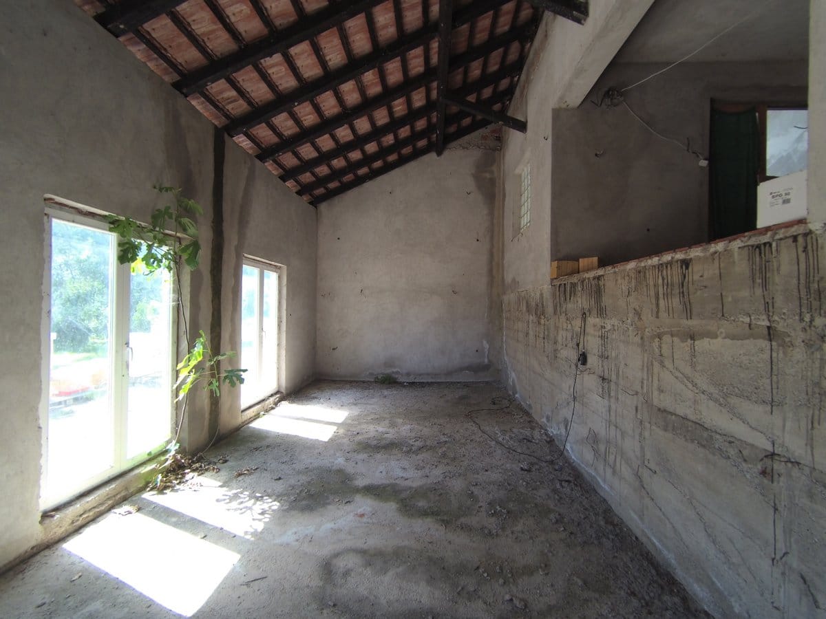 Shell finish house in Kavac, Montenegro: attic room with concrete walls and exposed roof beams.