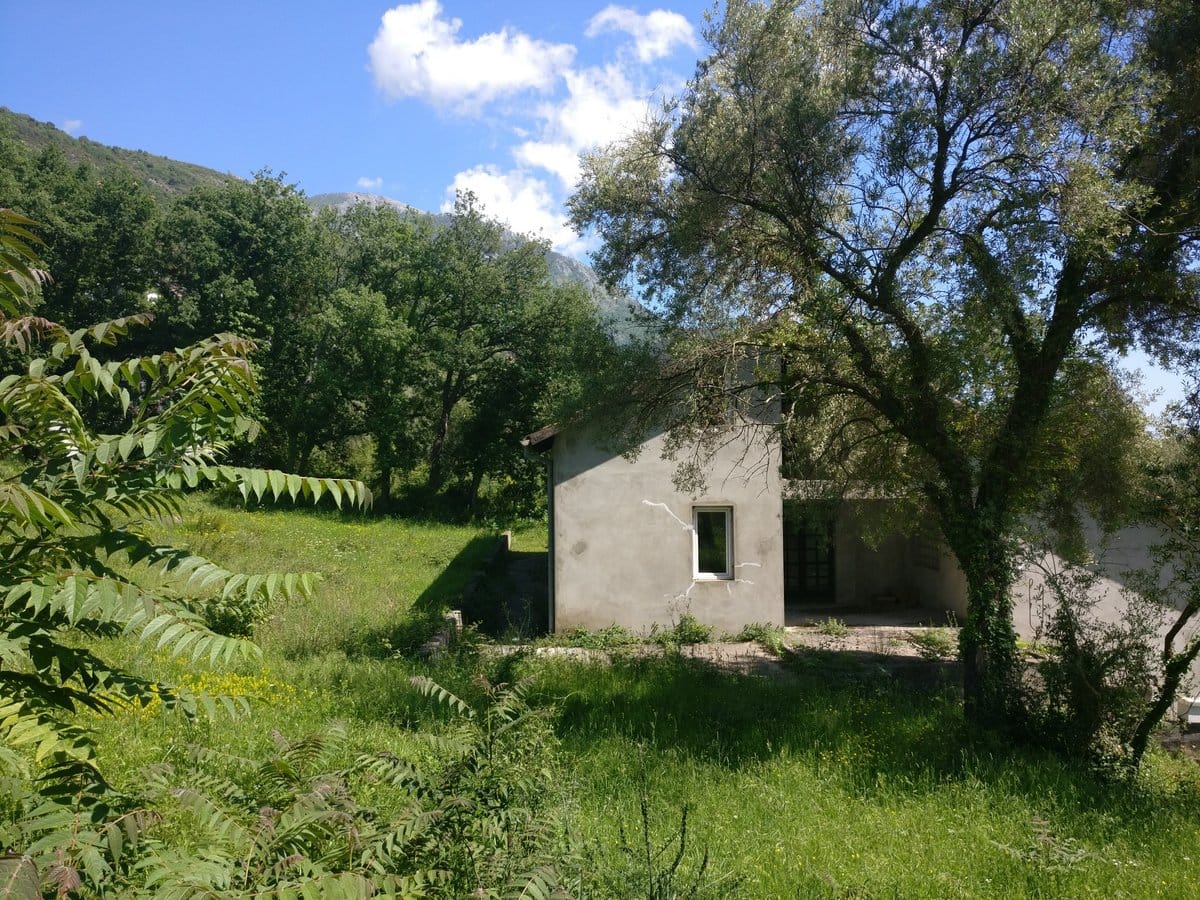 Private house with a plot surrounded by greenery and mountains in the village of Kavac, Montenegro, exterior view of the building facade.