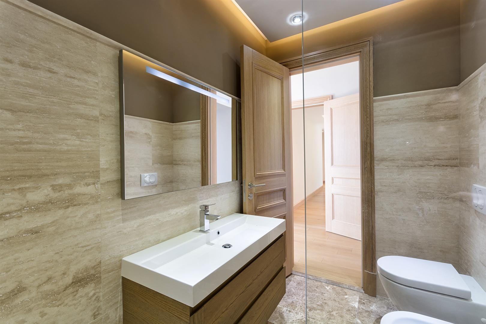 Modern bathroom with travertine finishes in Villa No. 154, Blizikuće, Montenegro: vanity, mirror, and sanitary ware.