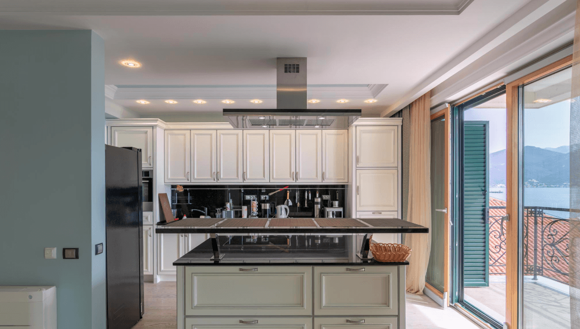Modern kitchen with island and sea view in a villa, Bijela, Montenegro: light-colored cabinetry, black backsplash, and appliances.