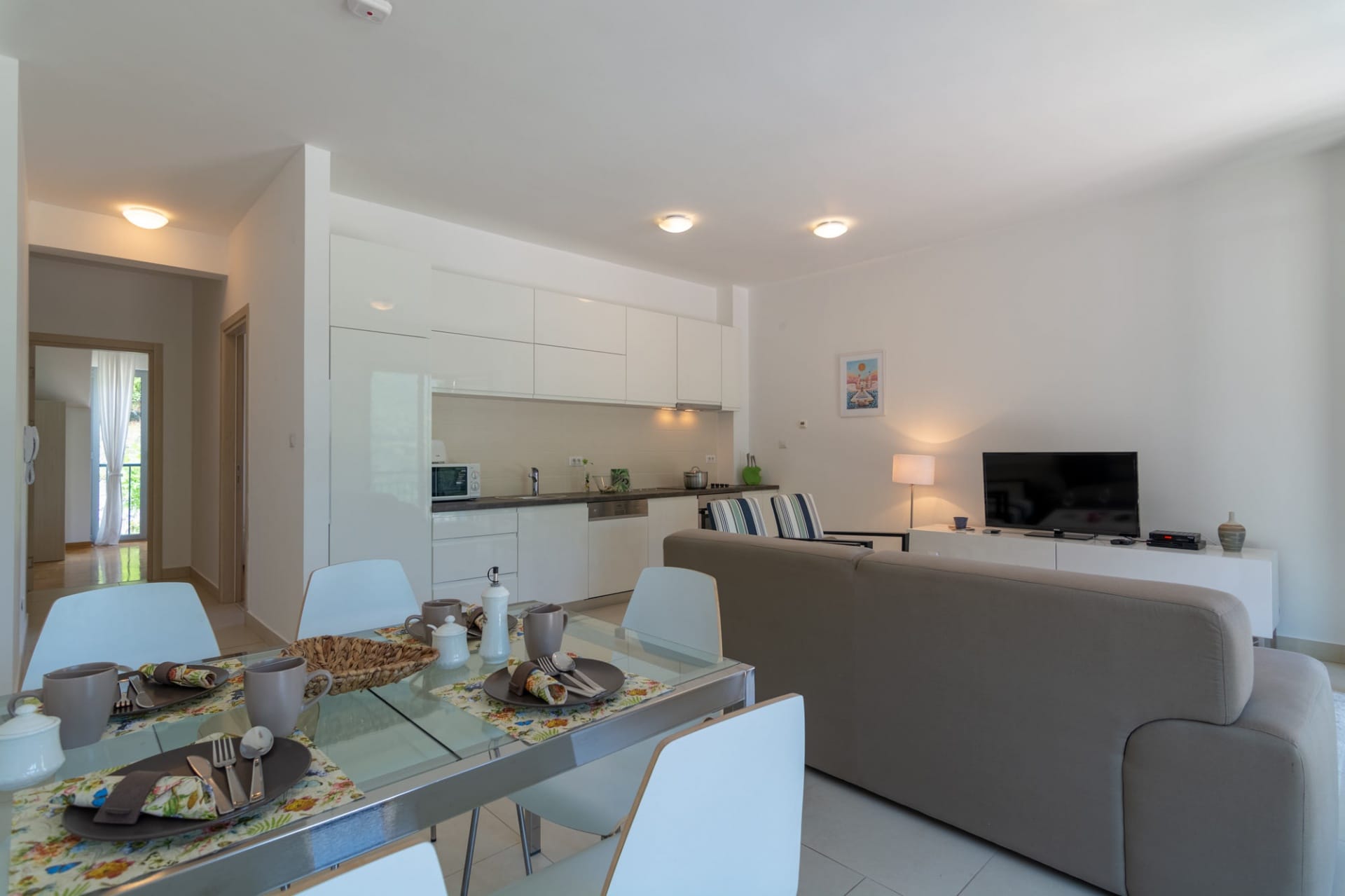 Modern living room with kitchen in an apartment, Morinj, Montenegro: dining table, light furniture, and TV area.