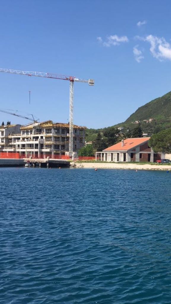 Residential complex under construction on the seafront in Đenovići, Montenegro: view of the property and the pier from the water.