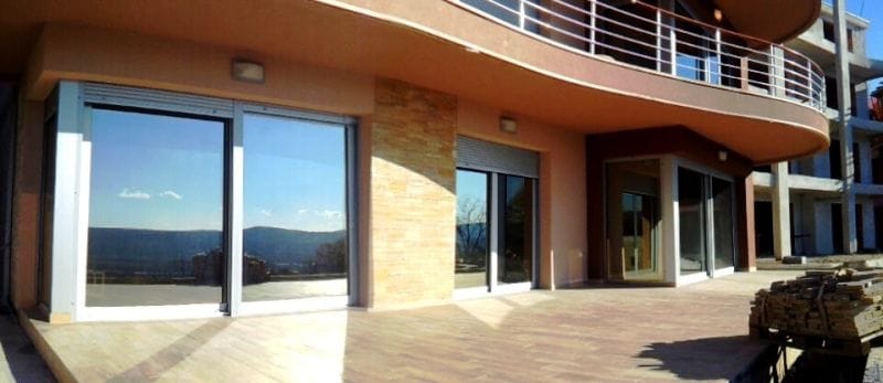Terrace of a modern apartment in Kavac, Montenegro: panoramic glazing, stone facade finish, and mountain views.
