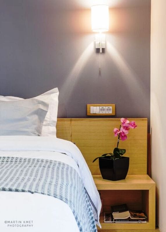 Modern bedroom in an apartment, Kavač, Montenegro: wooden bedside table, orchid, wall lamp, and a cozy bed.