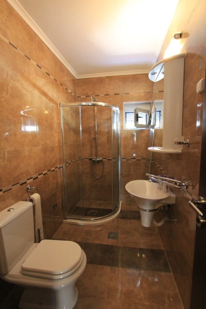 Bathroom with a shower cabin and white sanitary ware in a mini-hotel, Orahovac, Montenegro. Finished with beige tiles.