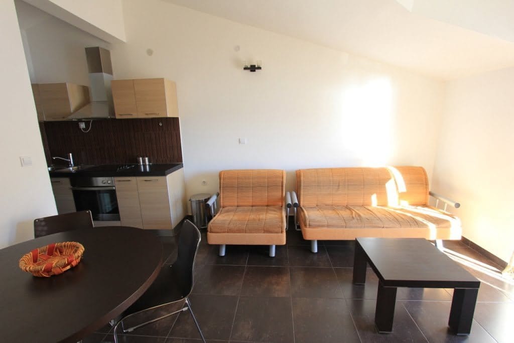 Living room with kitchen in a mini-hotel in Orahovac, Montenegro: orange sofas, dining table, and modern finishes.