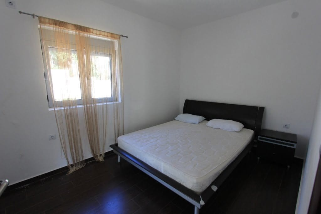 Bright bedroom with a double bed and dark floor in a mini-hotel, Orahovac, Montenegro. View of the window with tulle curtains.