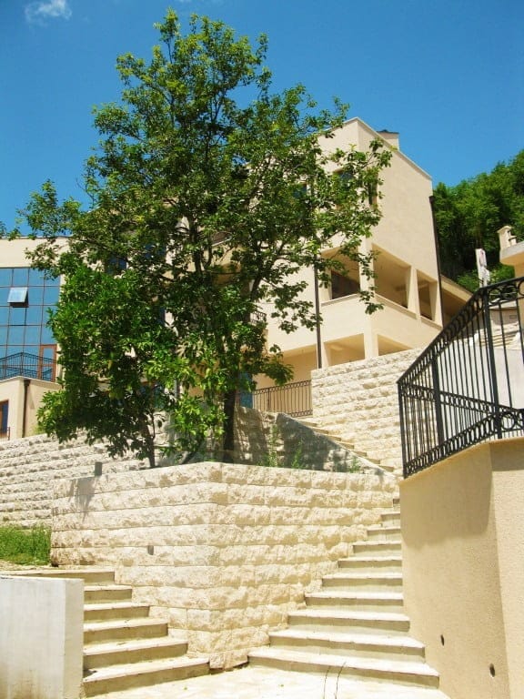Modern residential complex in Igalo, Montenegro: stone staircase, terraces, and a green tree by the building facade.