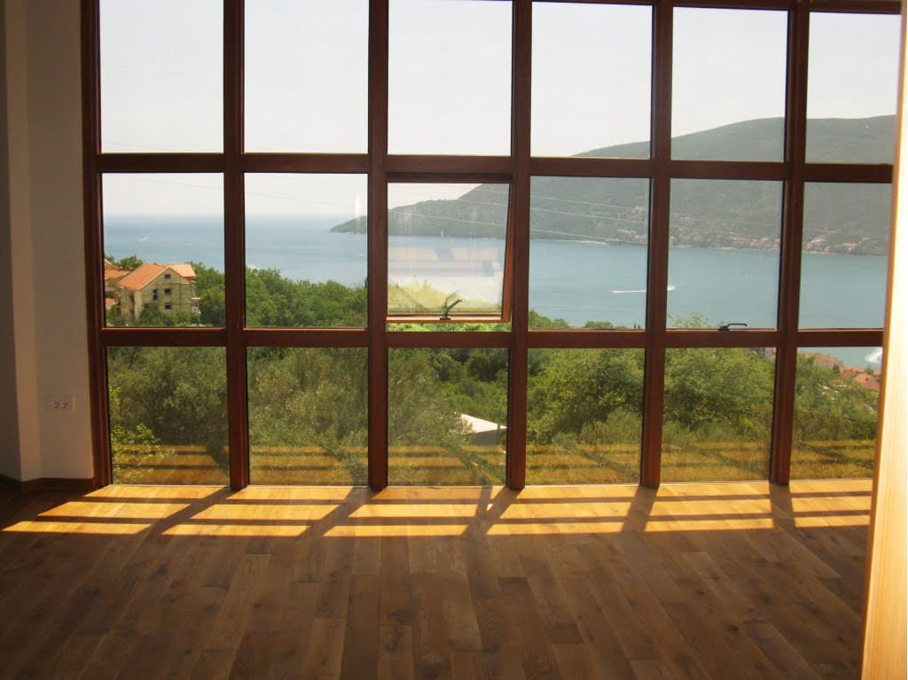 Panoramic window in the living room with a view of the sea and mountains, Igalo, Montenegro. Bright room with wooden flooring.