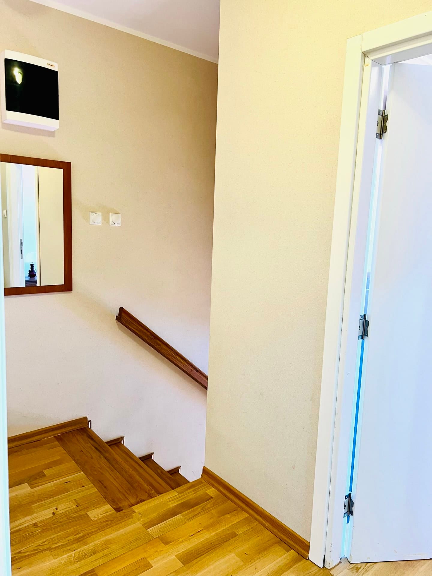 Bright staircase interior in a duplex, Petrovac, Montenegro: wooden steps, railing, and a wall mirror in the hallway.