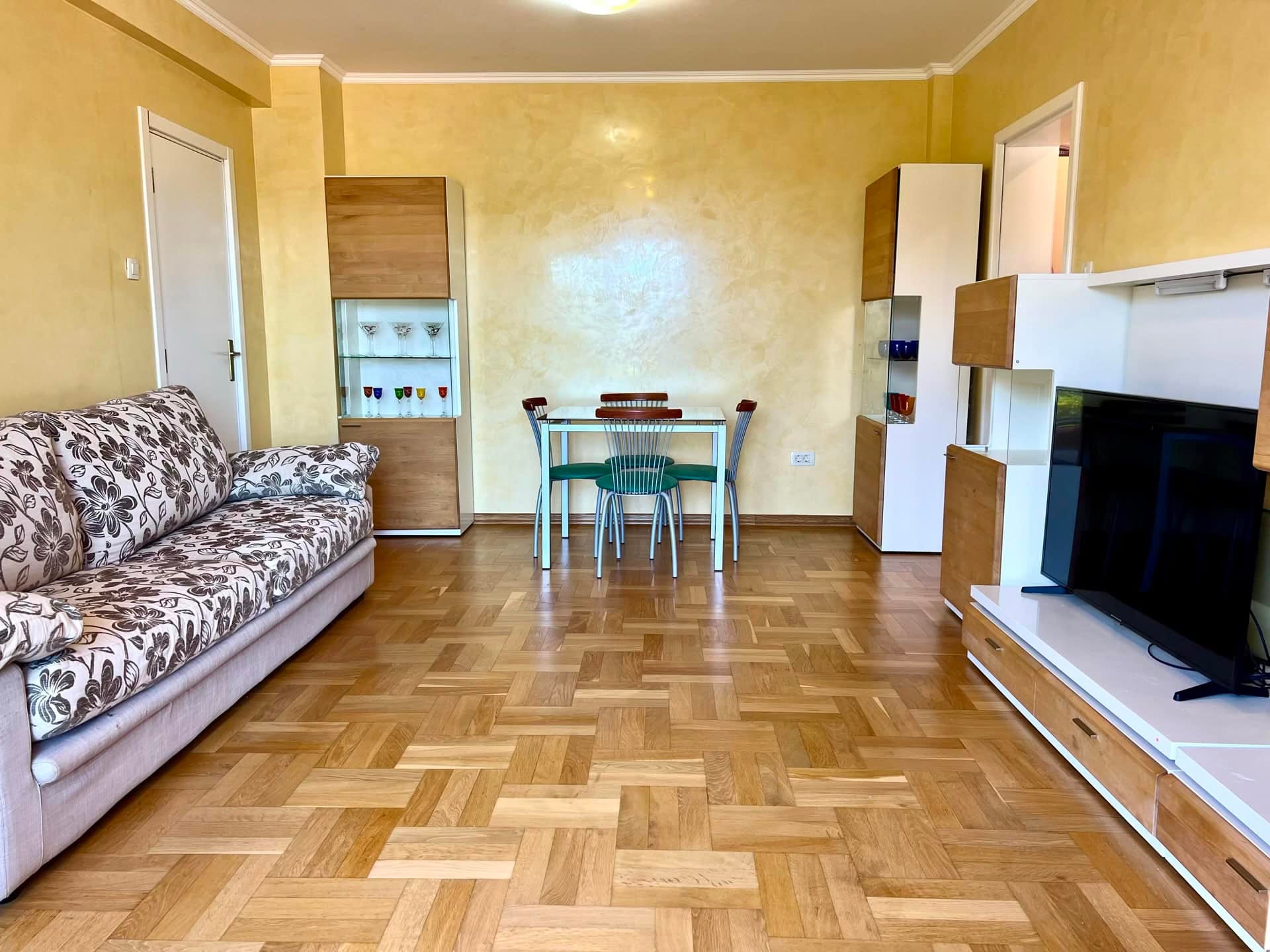 Living room in an apartment in Petrovac, Montenegro: parquet flooring, a soft sofa, a dining area, and a modern TV wall unit.