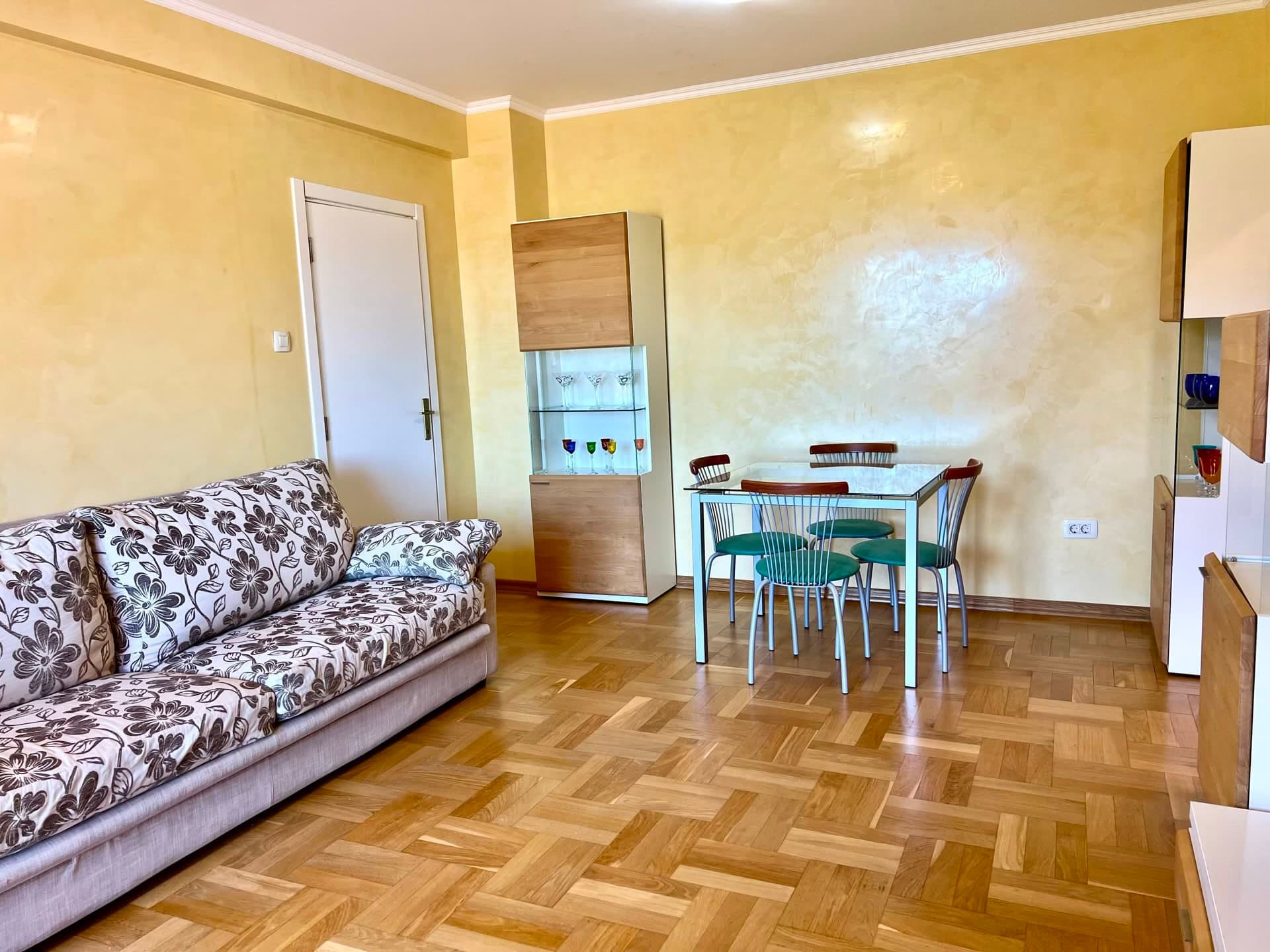 Living room in an apartment in Petrovac, Montenegro: floral-print sofa, dining area, and parquet flooring.