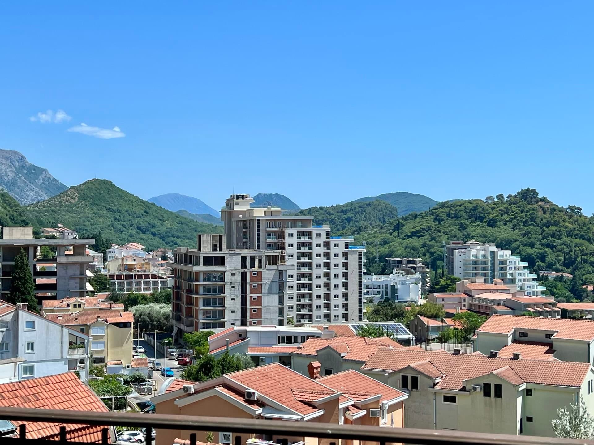 Panoramic view of the city of Petrovac in Montenegro with residential buildings, tiled roofs, and green mountains in the background.