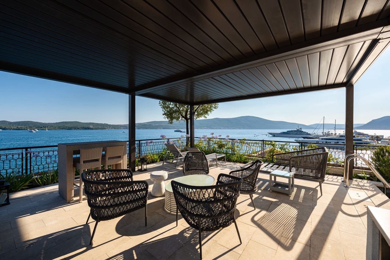 Terrace with wicker furniture in Porto Montenegro, Tivat, Montenegro: sea, yachts, and mountain views from a covered area.