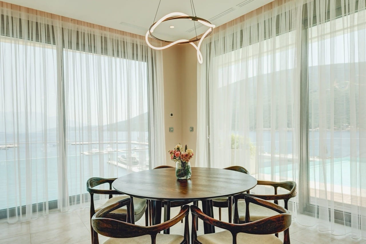 Dining area in an apartment in Portonovi, Kumbor, Montenegro: round table, designer chandelier, and a view of the marina.