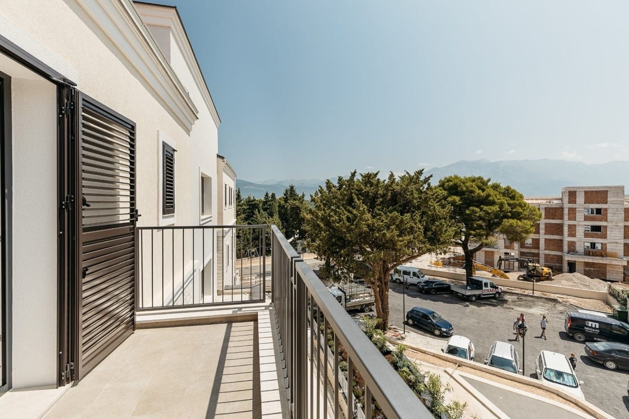 Balcony of a modern apartment in Luštica Bay, Radovići, Montenegro, with a view of the mountains and the residential complex parking area.