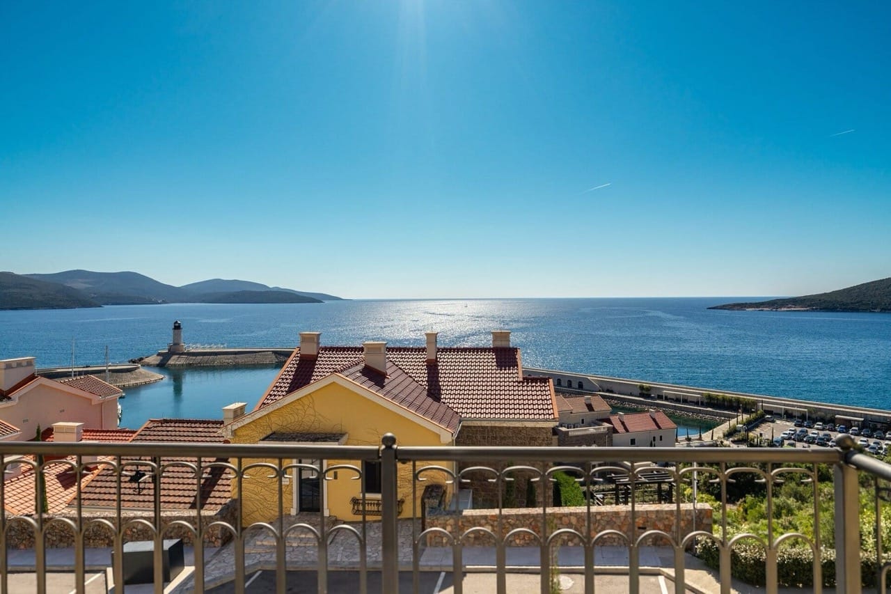 View from the villa balcony in Lustica Bay, Radovici, Montenegro: a panorama of the sea, lighthouse, and Mediterranean houses.