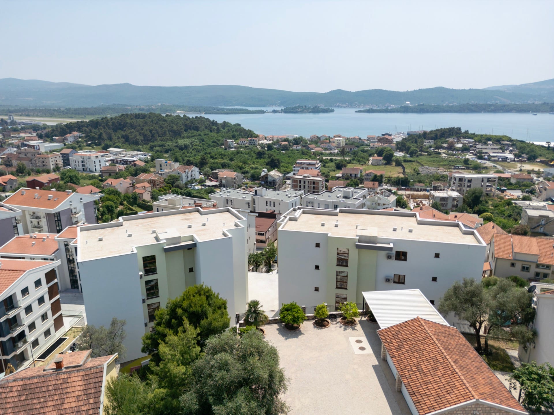 Aerial view of modern residential complexes in Tivat, Montenegro, with panoramic views of the sea and mountains.