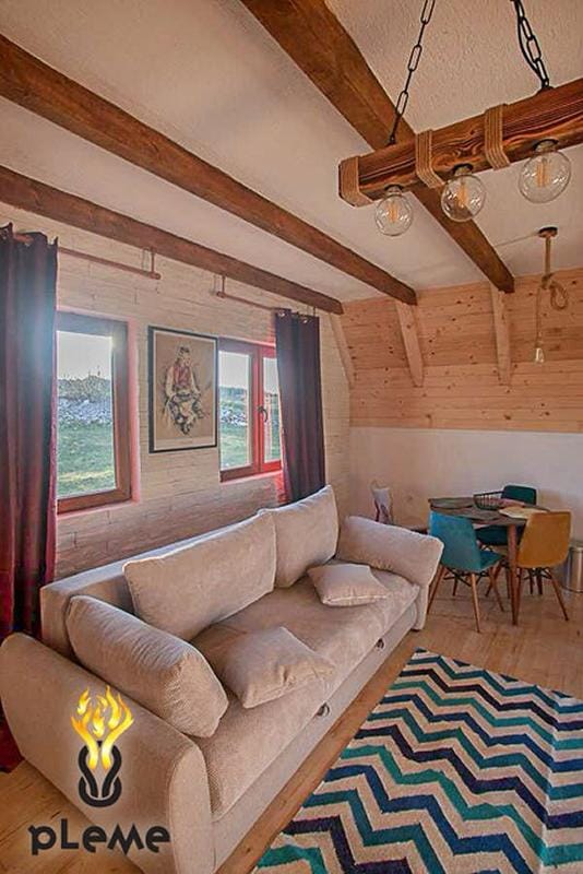 Rustic-style living room with wooden beams in a house, Žabljak, Montenegro: a soft sofa, dining area, and a view from the windows.