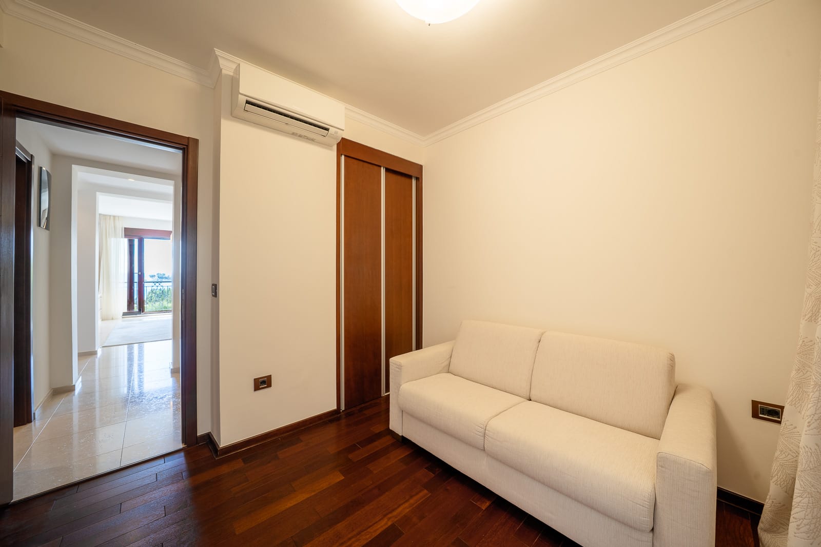 Bright living room with a white sofa and wooden cabinet in an apartment in Petrovac, Montenegro, with a view of the terrace.