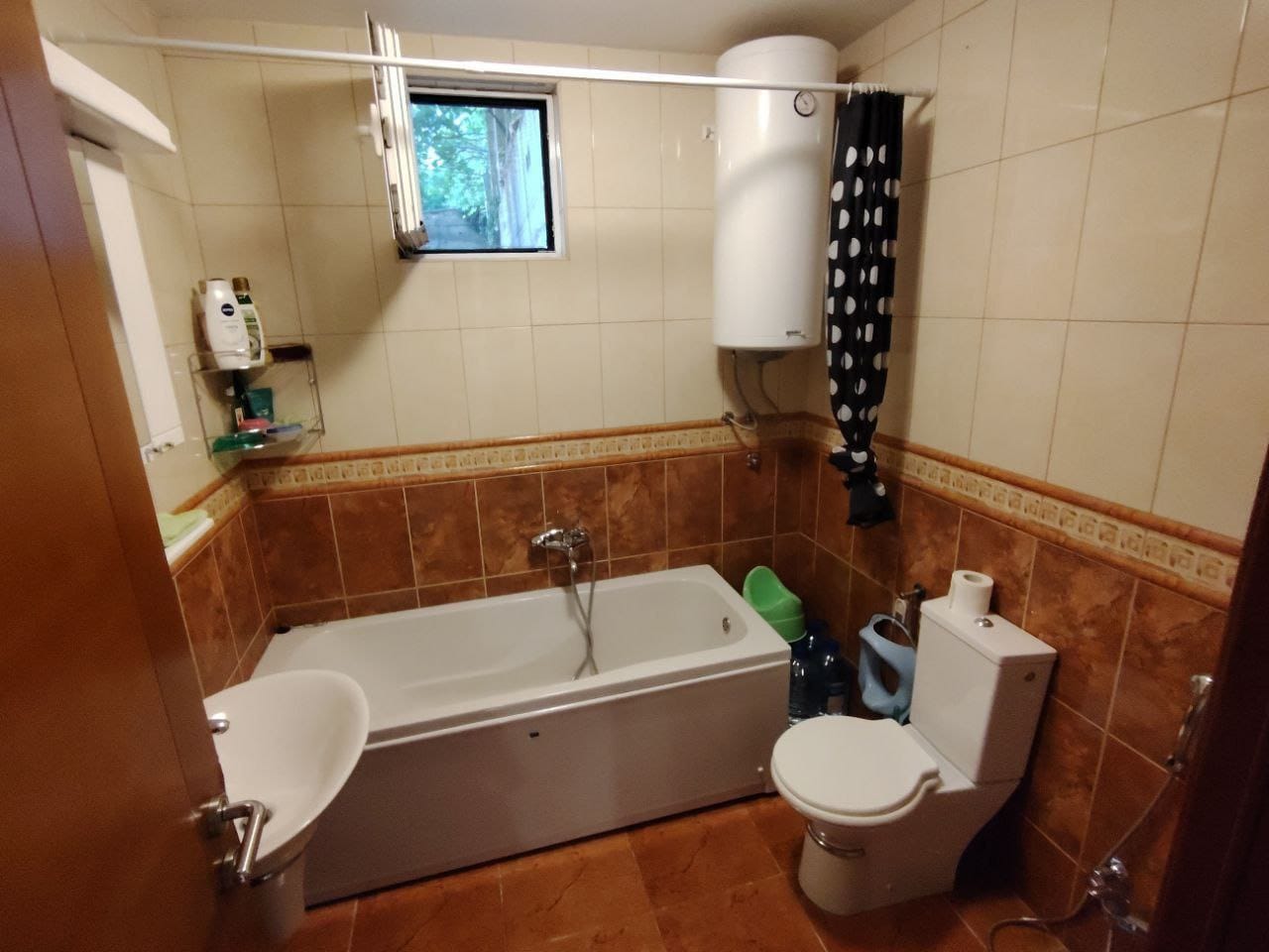 Bathroom in an apartment in Sutomore, Montenegro: tile, bathtub, water heater, toilet, and a window for ventilation.