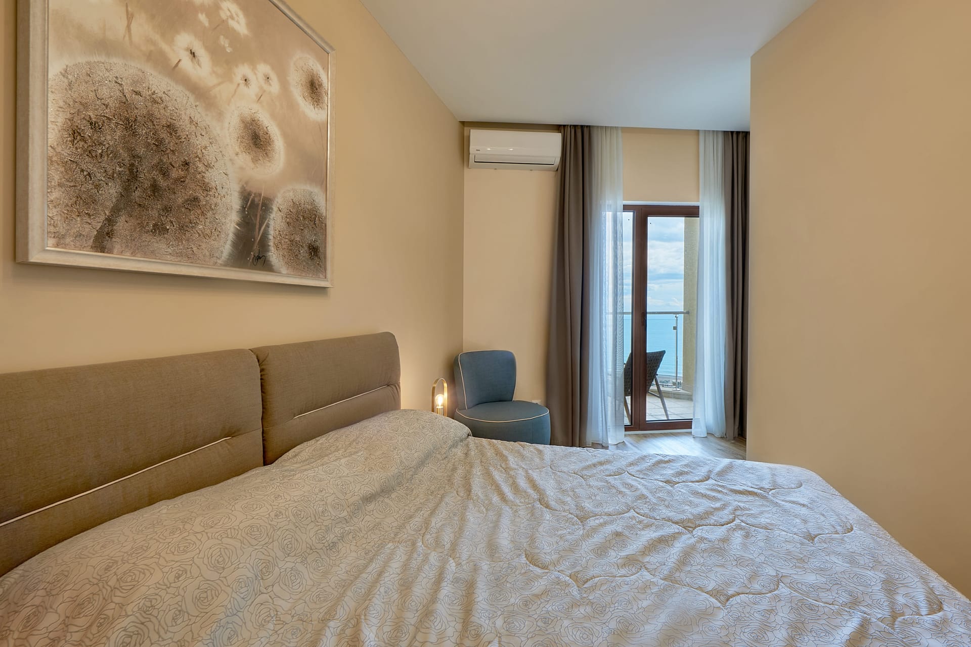 Bedroom in an apartment in Bečići, Montenegro: double bed, armchair, and access to a balcony with a sea view.