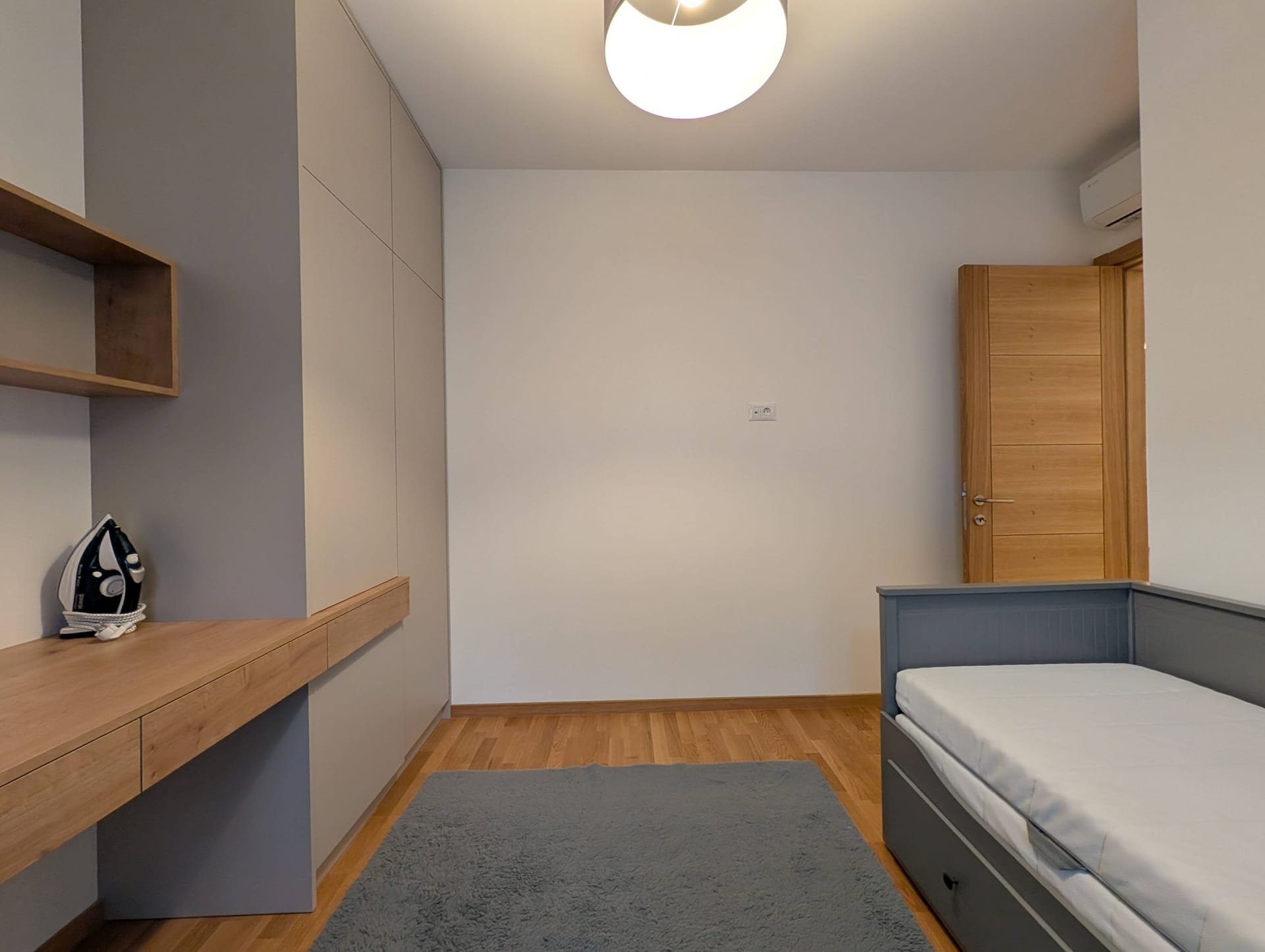 Modern bedroom in an apartment in Bečići, Montenegro: built-in wardrobe, desk, bed, and parquet flooring.