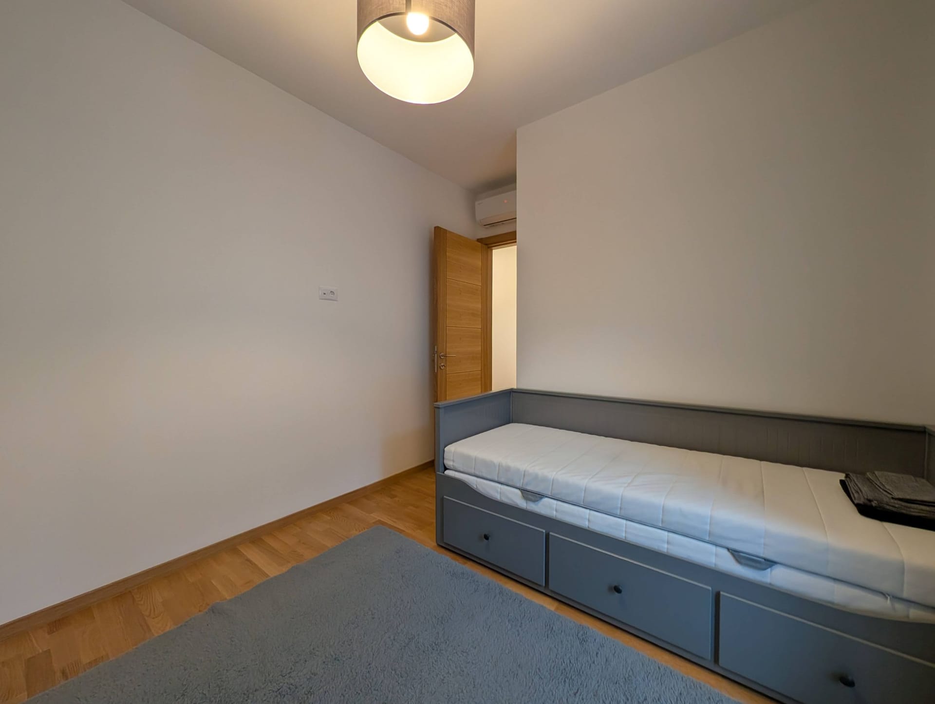 Bright bedroom with a gray bed and parquet flooring in an apartment in Bečići, Montenegro. Modern interior with air conditioning.