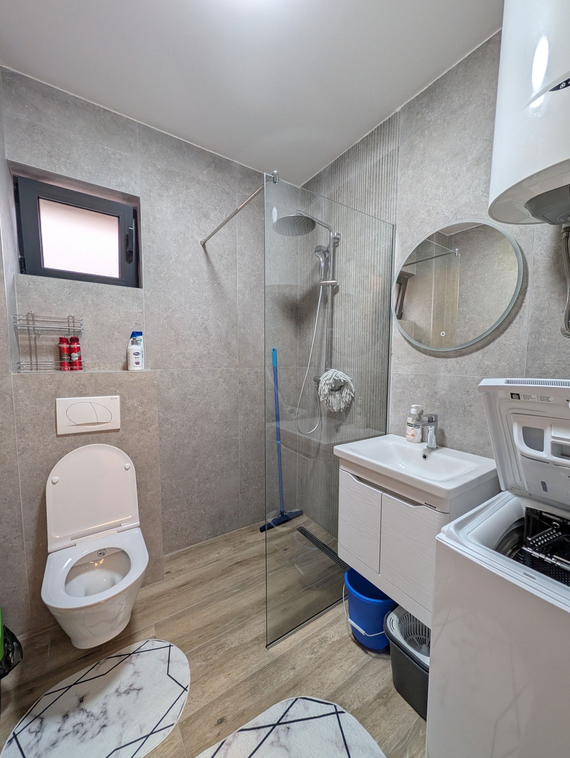 Modern bathroom in an apartment, Bečići, Montenegro: shower cabin, washing machine, and gray tiles.