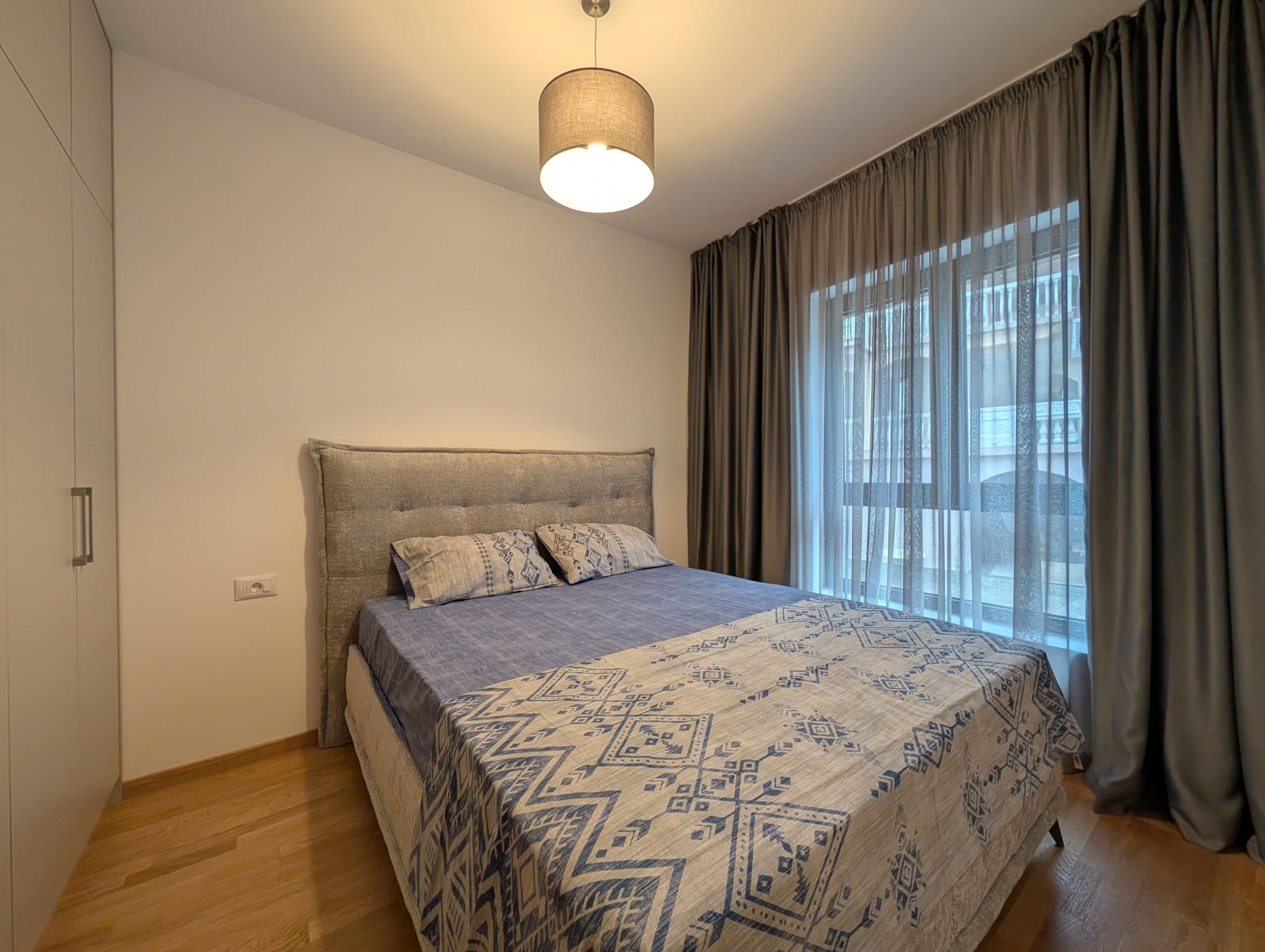 Modern bedroom with a double bed in an apartment in Bečići, Montenegro: bright interior, parquet flooring, and curtains.