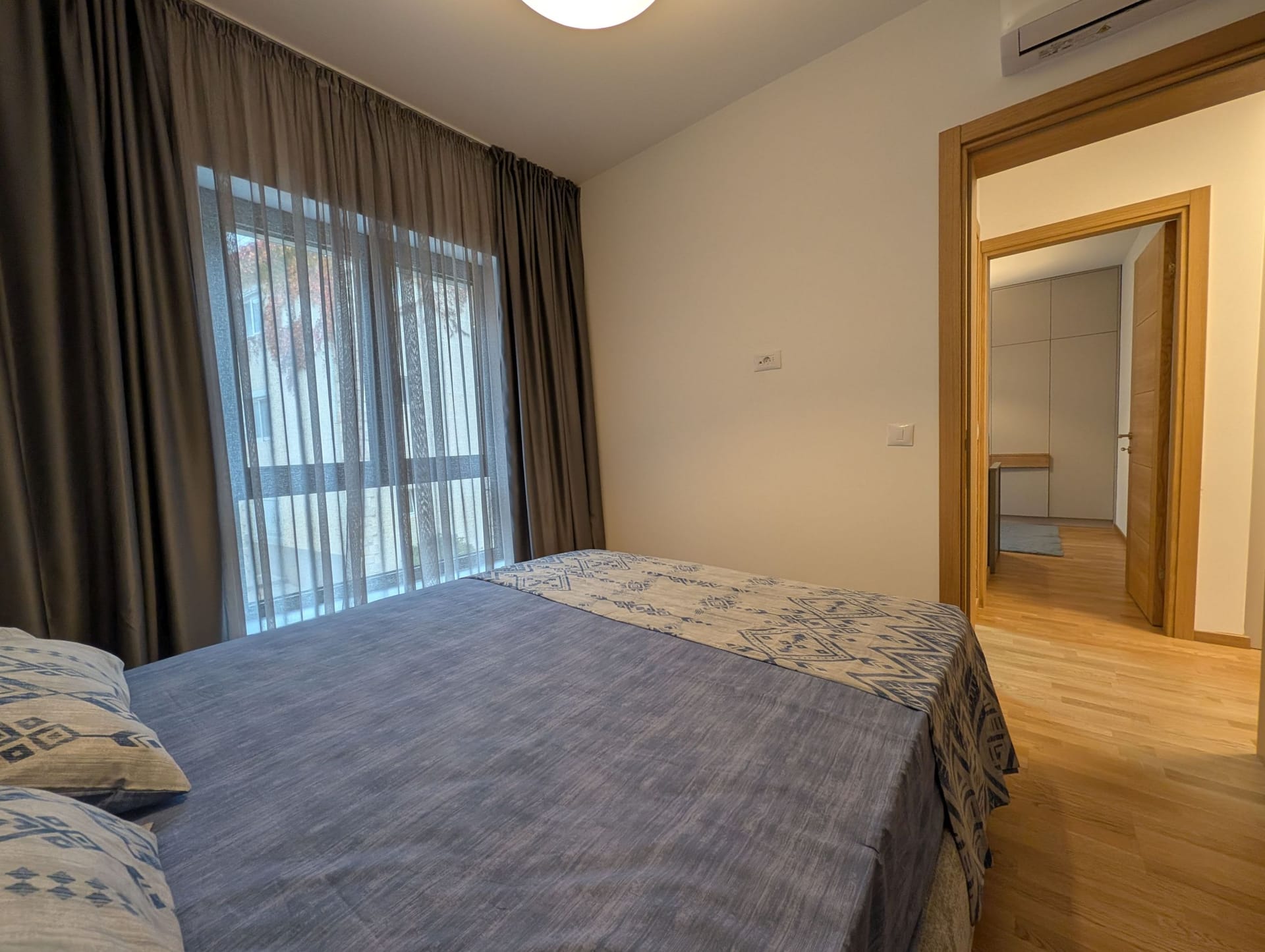 Modern bedroom with a double bed in an apartment in Bečići, Montenegro: light finishes and parquet flooring.