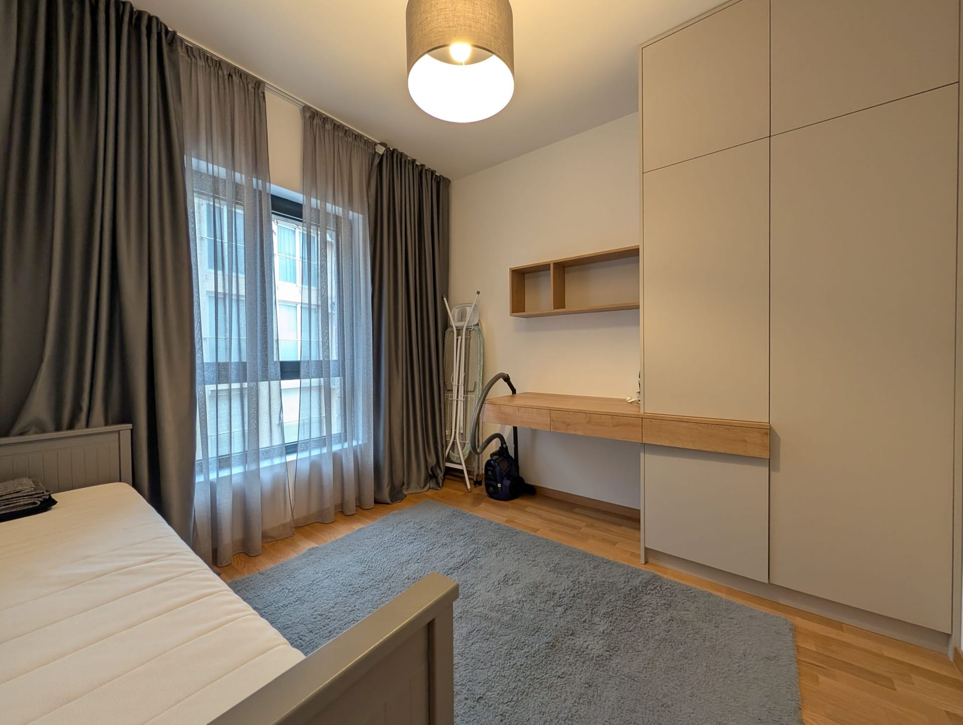 Modern bedroom in an apartment in Bečići, Montenegro: bed, built-in wardrobe, desk, and gray curtains.