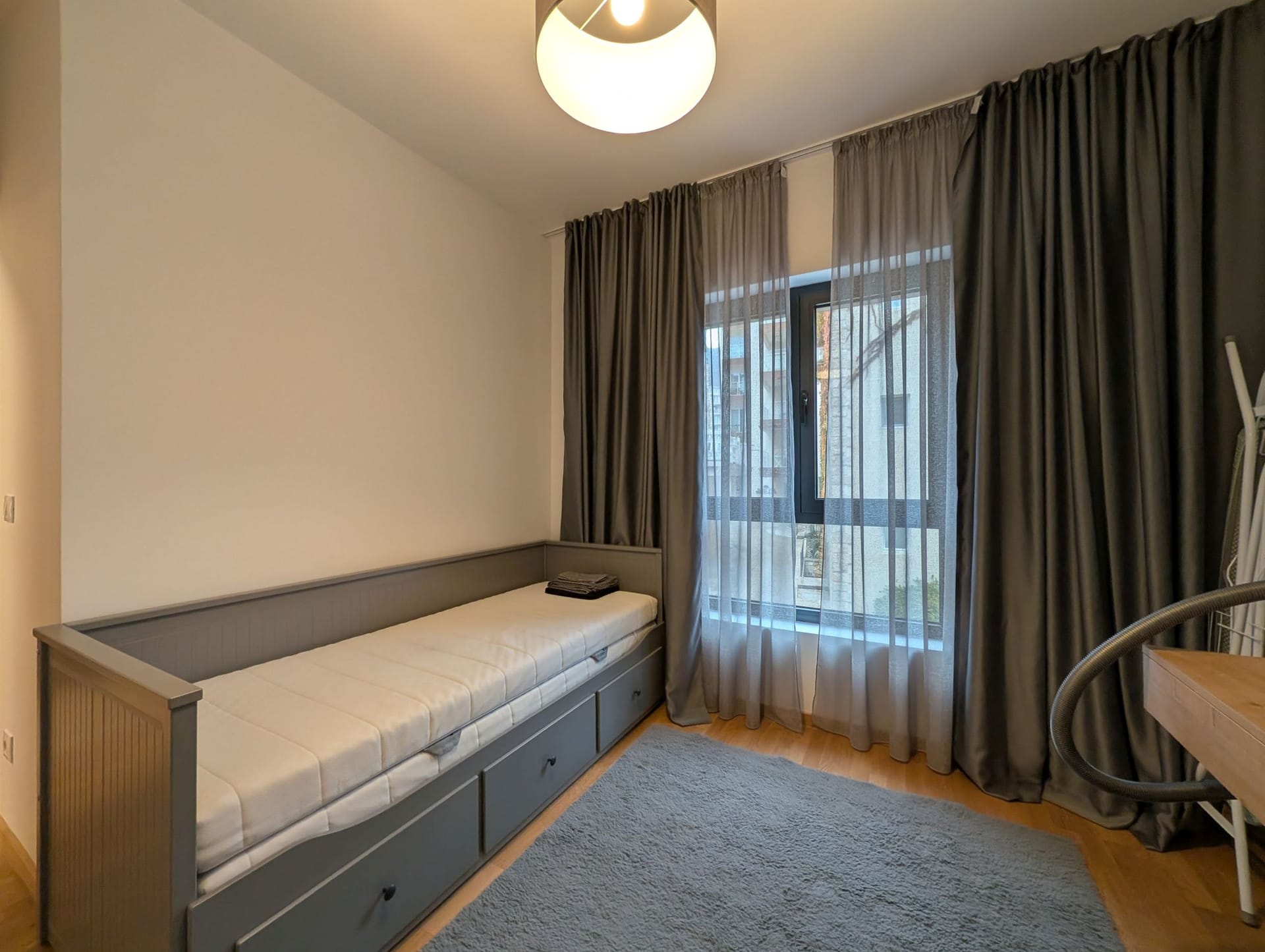 Bedroom with a gray bed and blackout curtains in an apartment in Bečići, Montenegro. Modern interior with a carpet.