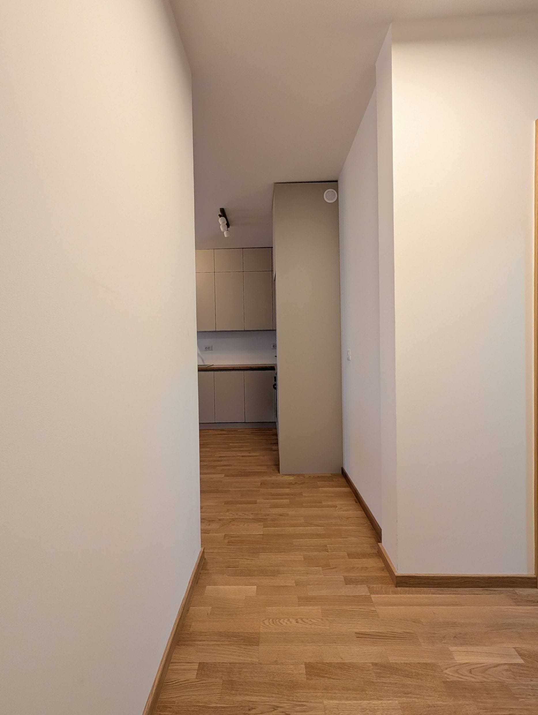 Modern kitchen in light tones with wooden flooring in an apartment, Bečići, Montenegro. View from the hallway onto the kitchen unit.