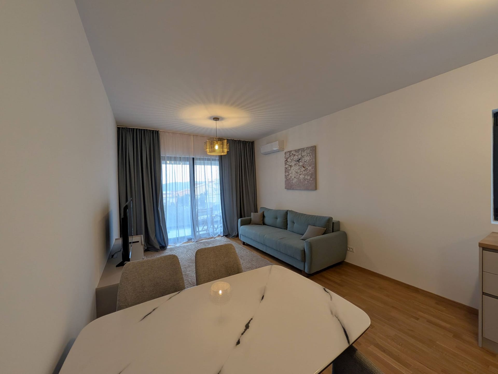 Modern living room in Bečići apartments, Montenegro: dining table, grey sofa, panoramic window, and stylish decor.