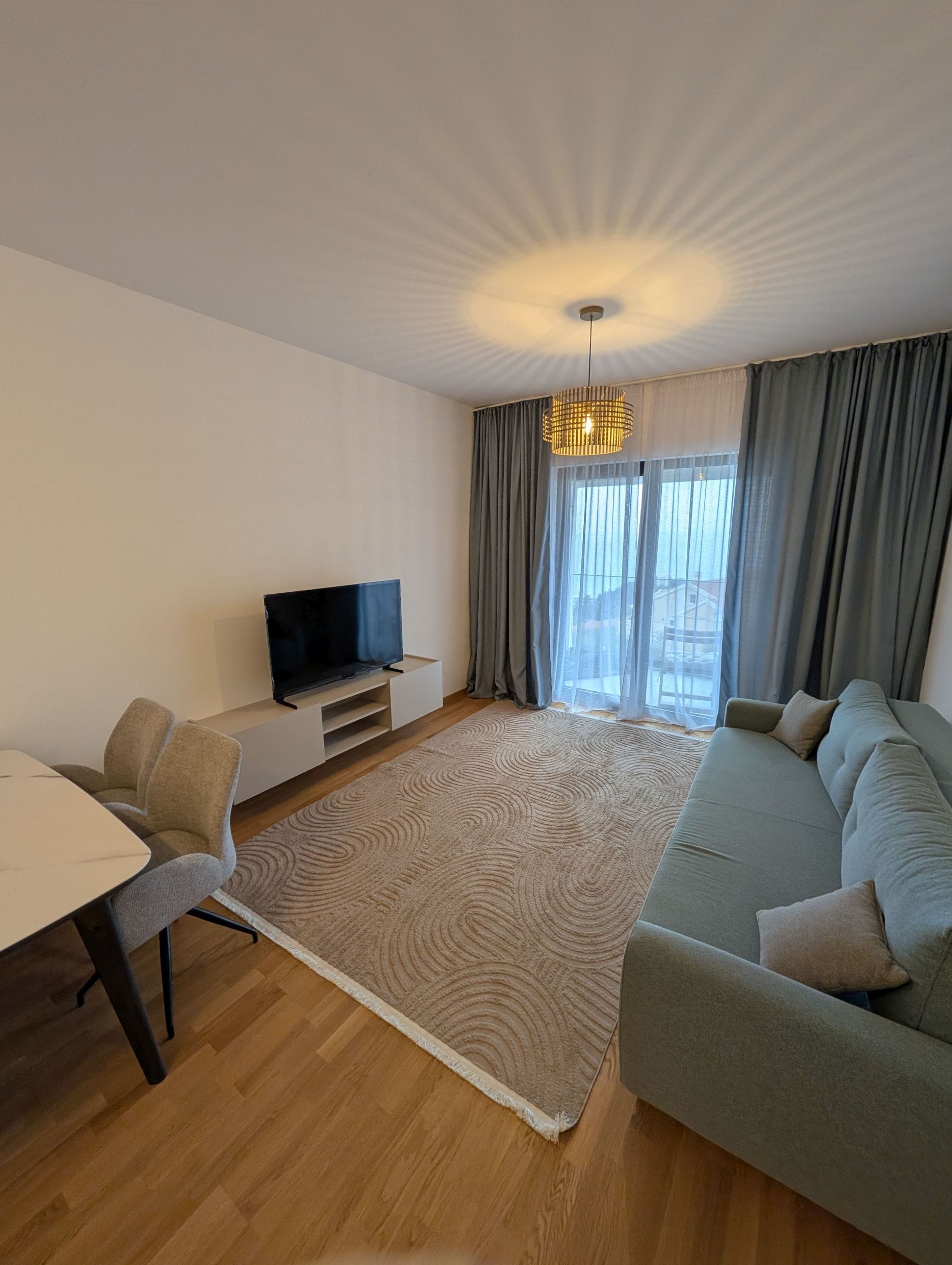 Modern living room in an apartment in Bečići, Montenegro: sofa, TV area, dining table, and access to a balcony with a view.