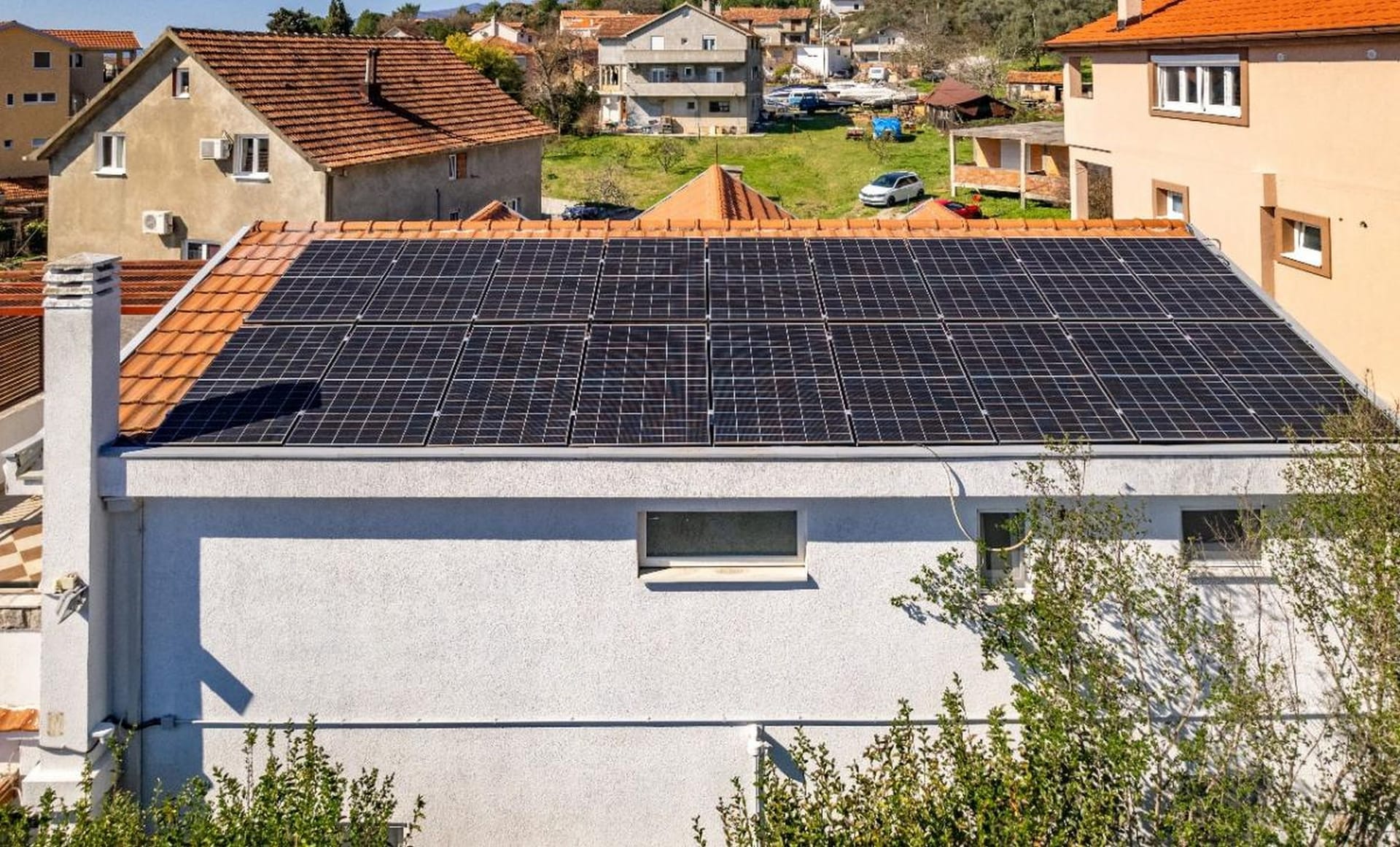 Modern solar panels on the roof of a private house in Tivat, Montenegro, overlooking a residential area with tiled roofs.