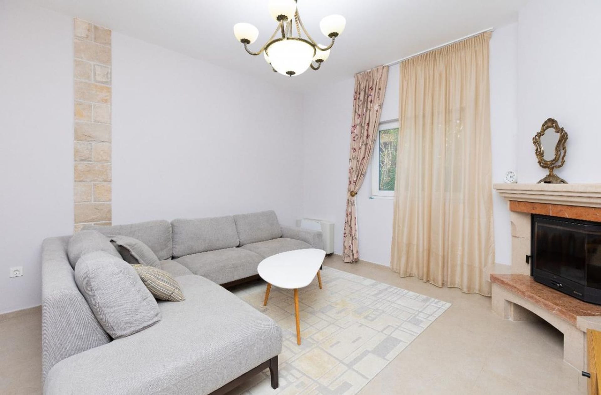 Living room in a house in Tivat, Montenegro: gray corner sofa, stone-clad fireplace, and a bright interior.