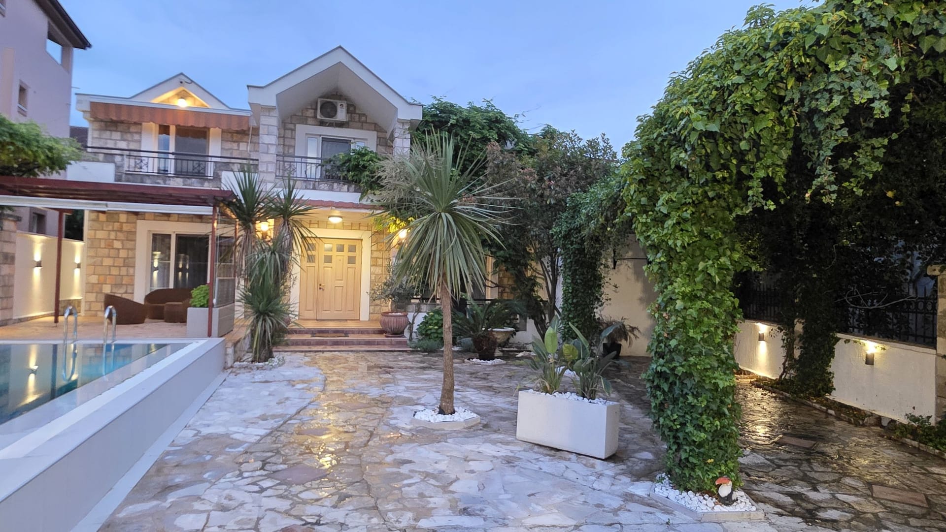 Two-story villa in Tivat, Montenegro: stone facade, swimming pool, well-kept garden with palm trees, and a cozy terrace.