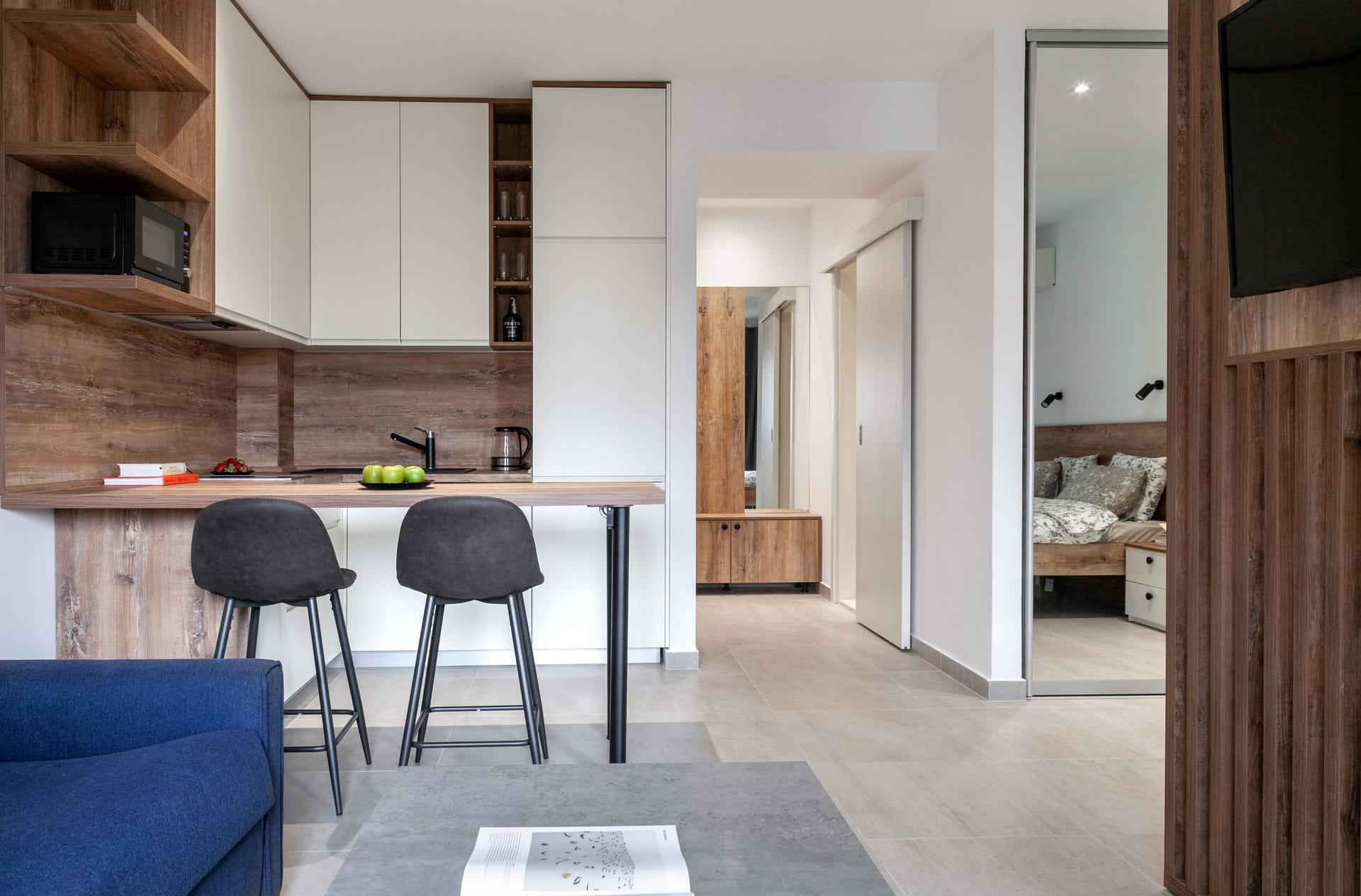 Modern studio kitchen with a bar counter in an apartment in Kotor, Montenegro: light furniture, wood, and a view of the bedroom.