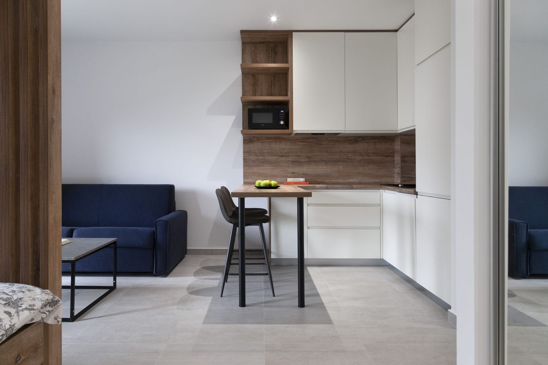Modern kitchen-living room in an apartment in Kotor, Montenegro: white cabinetry, a breakfast bar, and a blue sofa in the interior.