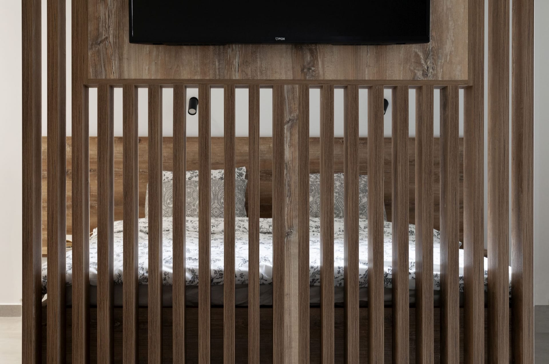 Modern bedroom in an apartment in Kotor, Montenegro: bed behind a decorative wooden partition with a TV panel.