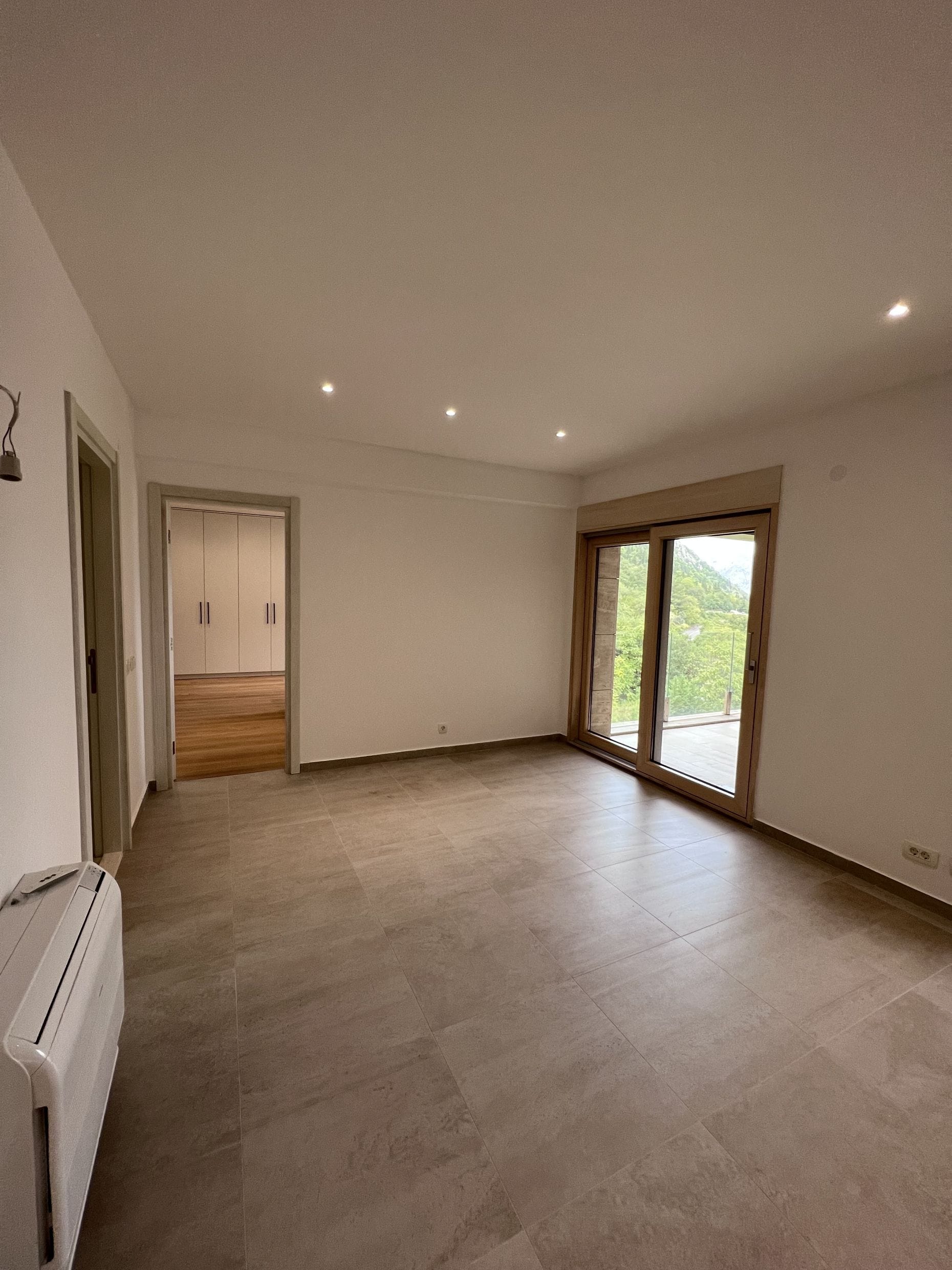 Bright living room with a panoramic window and mountain view in an apartment, Kotor, Montenegro. Modern finishes and tile.