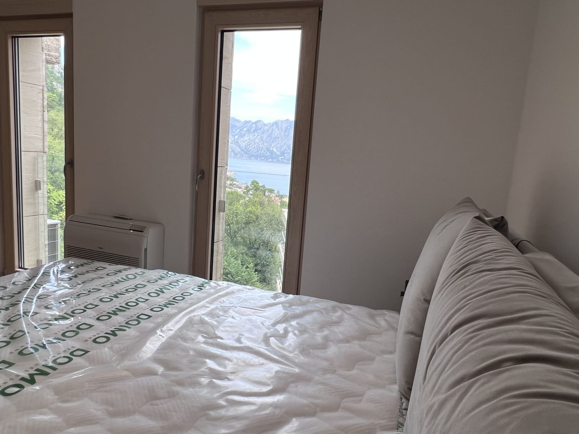 Bedroom in an apartment in Kotor, Montenegro, with panoramic views of Kotor Bay and the mountains through tall windows.