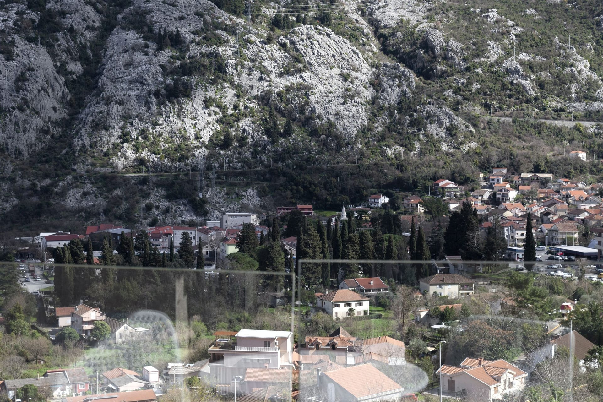 Panoramic view from the apartment window of the mountains and the city of Kotor in Montenegro from a terrace with glass railing.